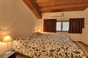 Un dormitorio con una cama, mesita de noche, lámpara, ventana con cortinas y equipo de aire acondicionado.
