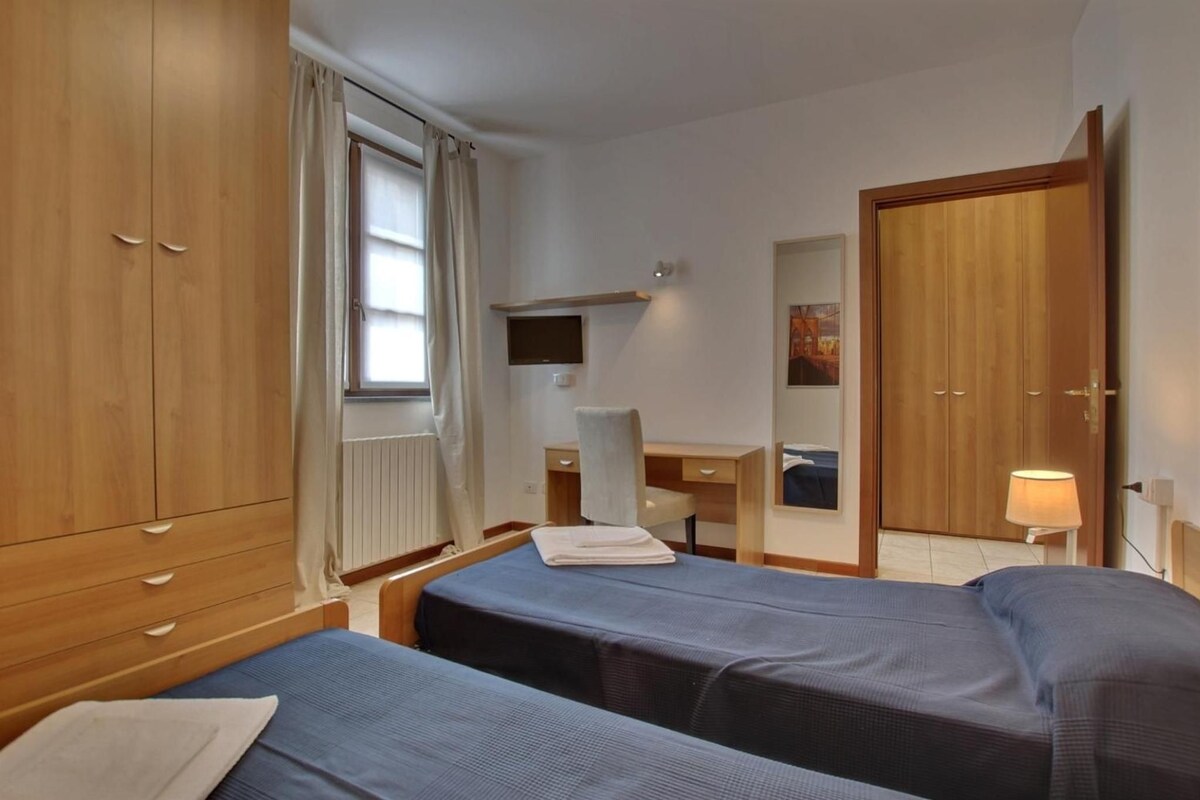 A room with two beds, a desk, a chair, a TV, and a wardrobe.