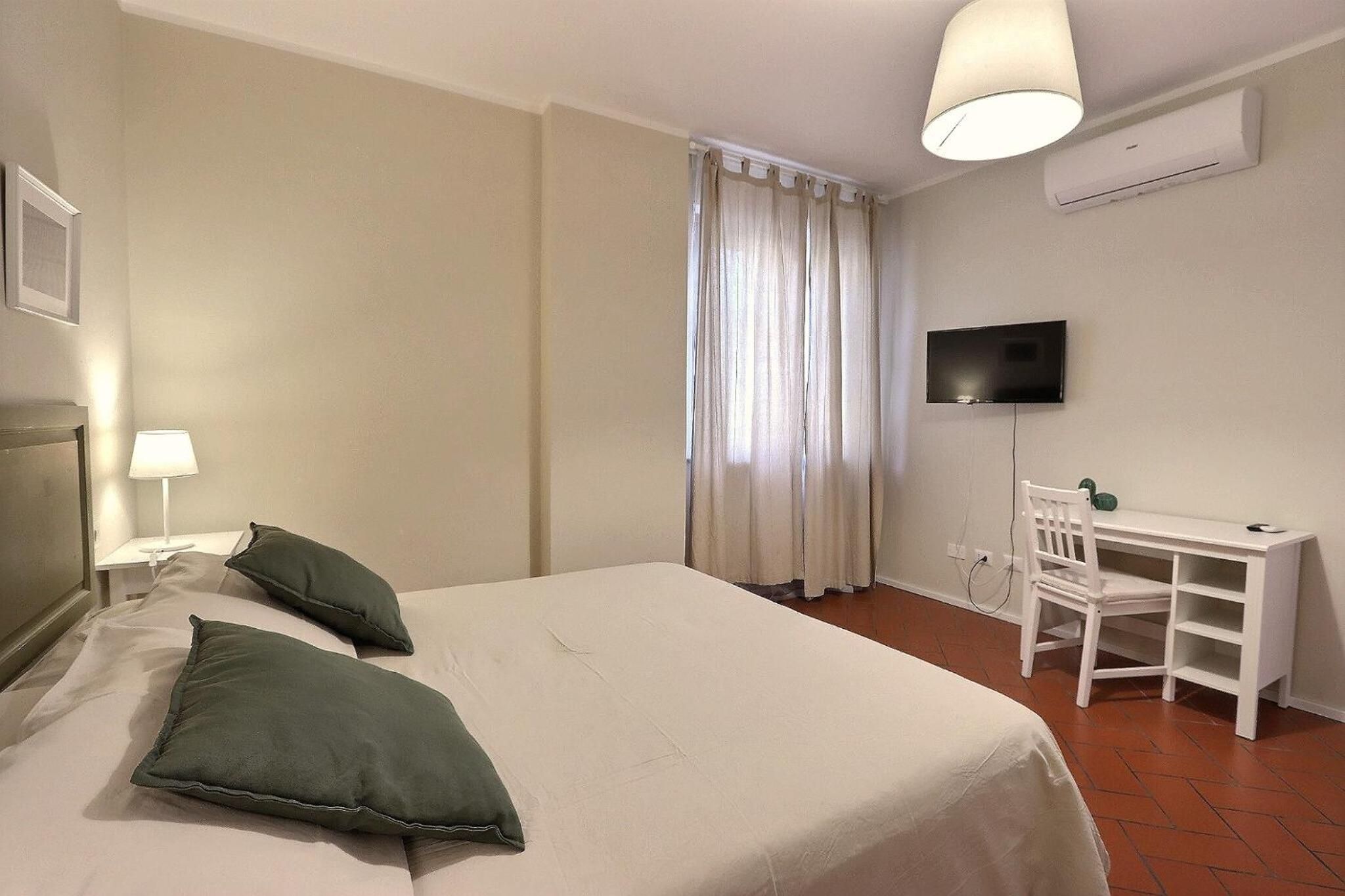 Una habitación de hotel con cama, escritorio, silla, televisor y ventana con cortinas.