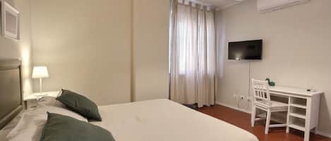 Una habitación de hotel con cama, escritorio, silla, televisor y ventana con cortinas.