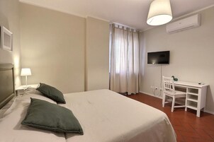Una habitación de hotel con cama, escritorio, silla, televisor y ventana con cortinas.