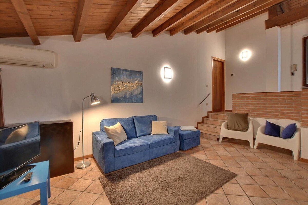 A living room with a blue sofa, a TV, a lamp, and a staircase leading to an upper level.