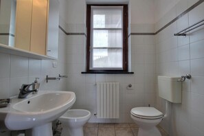 Un baño con inodoro, bidé y lavabo. Hay una ventana sobre el inodoro y un perchero debajo.