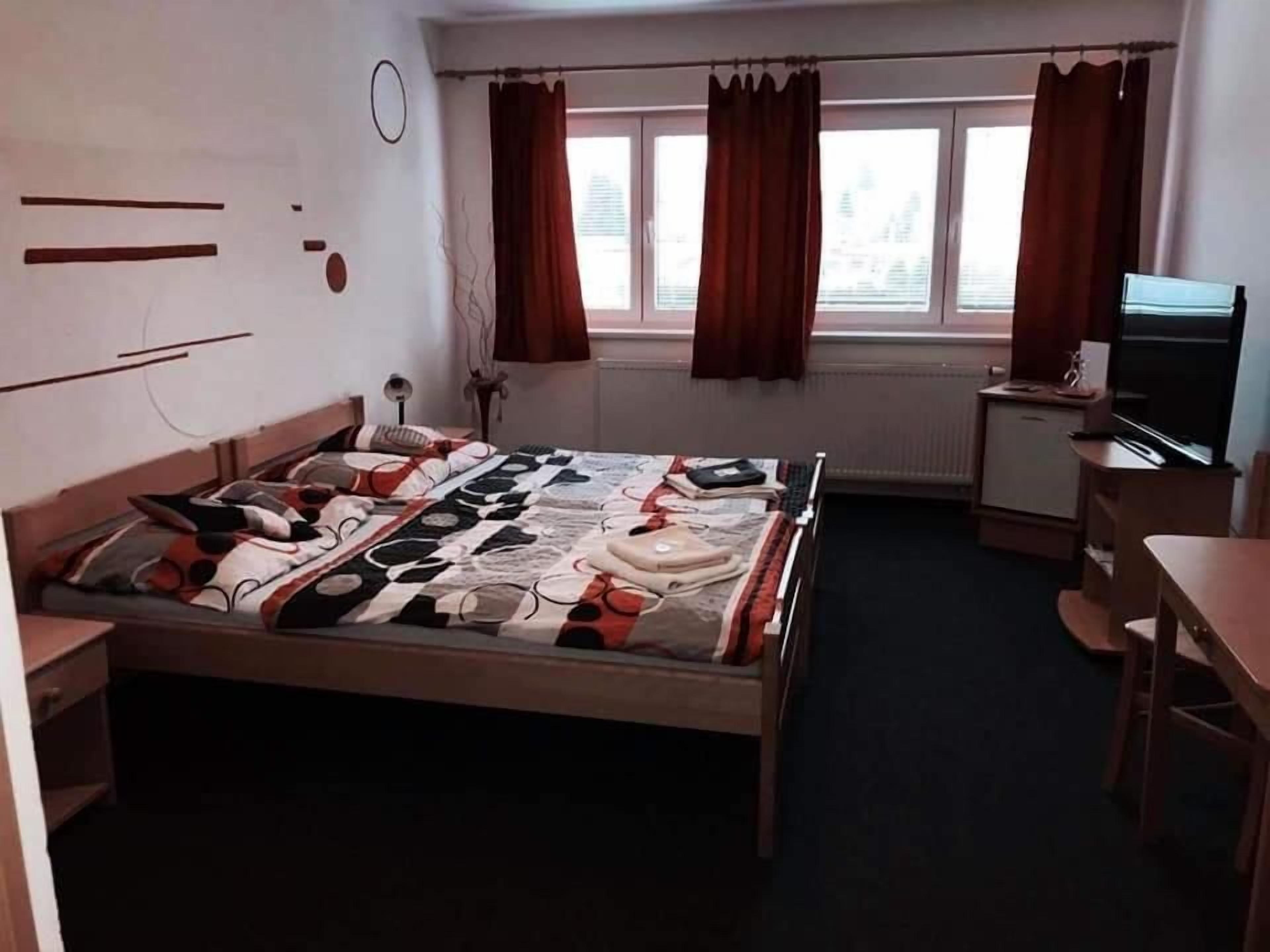 A bedroom with a bed, a desk, a chair, a television, and a window with curtains.