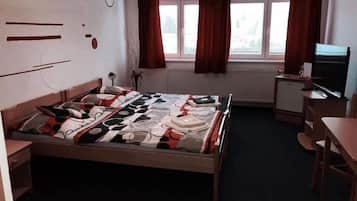 A bedroom with a bed, a desk, a chair, a television, and a window with curtains.