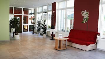 Um lobby amplo com um sofá vermelho, uma mesinha e plantas em vasos.