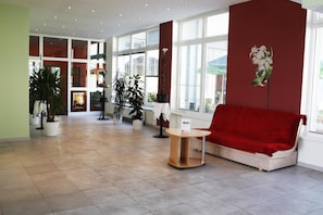 Un vestíbulo amplio con un sofá rojo, una mesita y plantas en macetas.