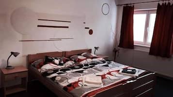 Quarto com cama, mesas de cabeceira, janela com cortinas e relógio na parede.