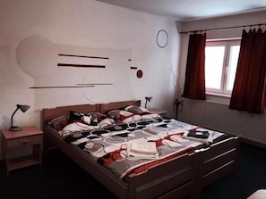 Un dormitorio con cama, mesitas de noche, una ventana con cortinas y un reloj de pared.