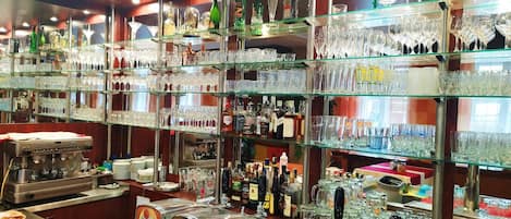 A bar area with multiple shelves of bottles and glasses, a coffee machine, and a tap labeled 'Kozel.'