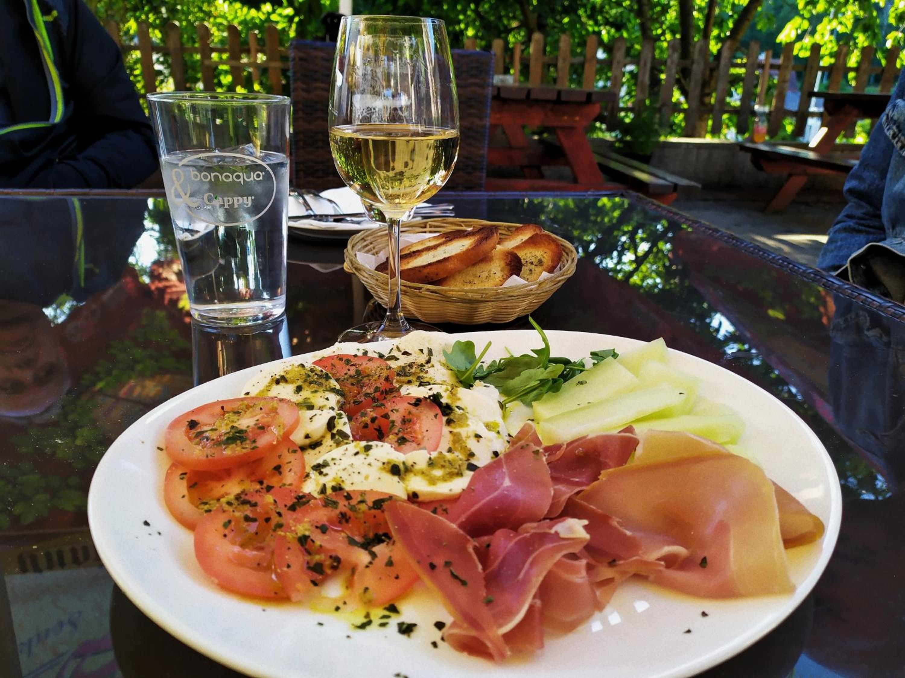 A glass table with a plate of food, a glass of water, and a glass of white wine.