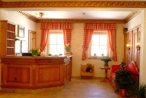 A cozy room with a wooden bar, two windows with red curtains, a red sofa, and a small table with a vase of flowers. - Landhaus Appartementhaus Haussteiner (Dorfgastein)