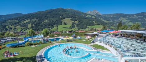 Una piscina con un diseño espiral único, rodeada de césped con sombrillas, con montañas como telón de fondo.