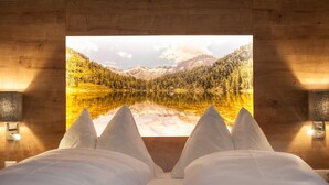 A bedroom with a bed facing a large window displaying a mountain landscape. - Landhaus Appartementhaus Haussteiner (Dorfgastein)