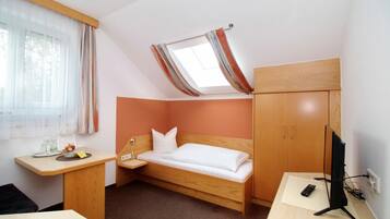 Ein kleines Hotelzimmer mit Bett, Schreibtisch, Fernseher und einem Fenster mit Vorhängen.