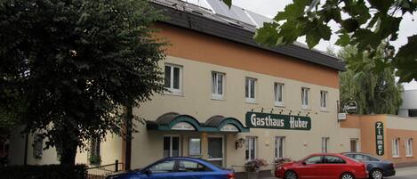 Un edificio con un letrero que dice 'Gasthaus Huber' y dos coches estacionados adelante.