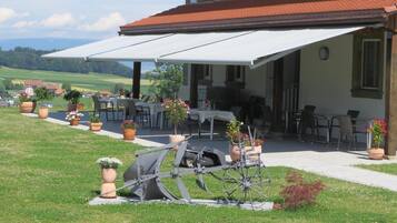 A covered outdoor seating area with tables and chairs, surrounded by potted plants.