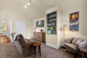 A living room with a sofa, a coffee table, a bookshelf, and a lamp. - The Farmhouse | Mountain Views + Room to Roam (Port Angeles East)