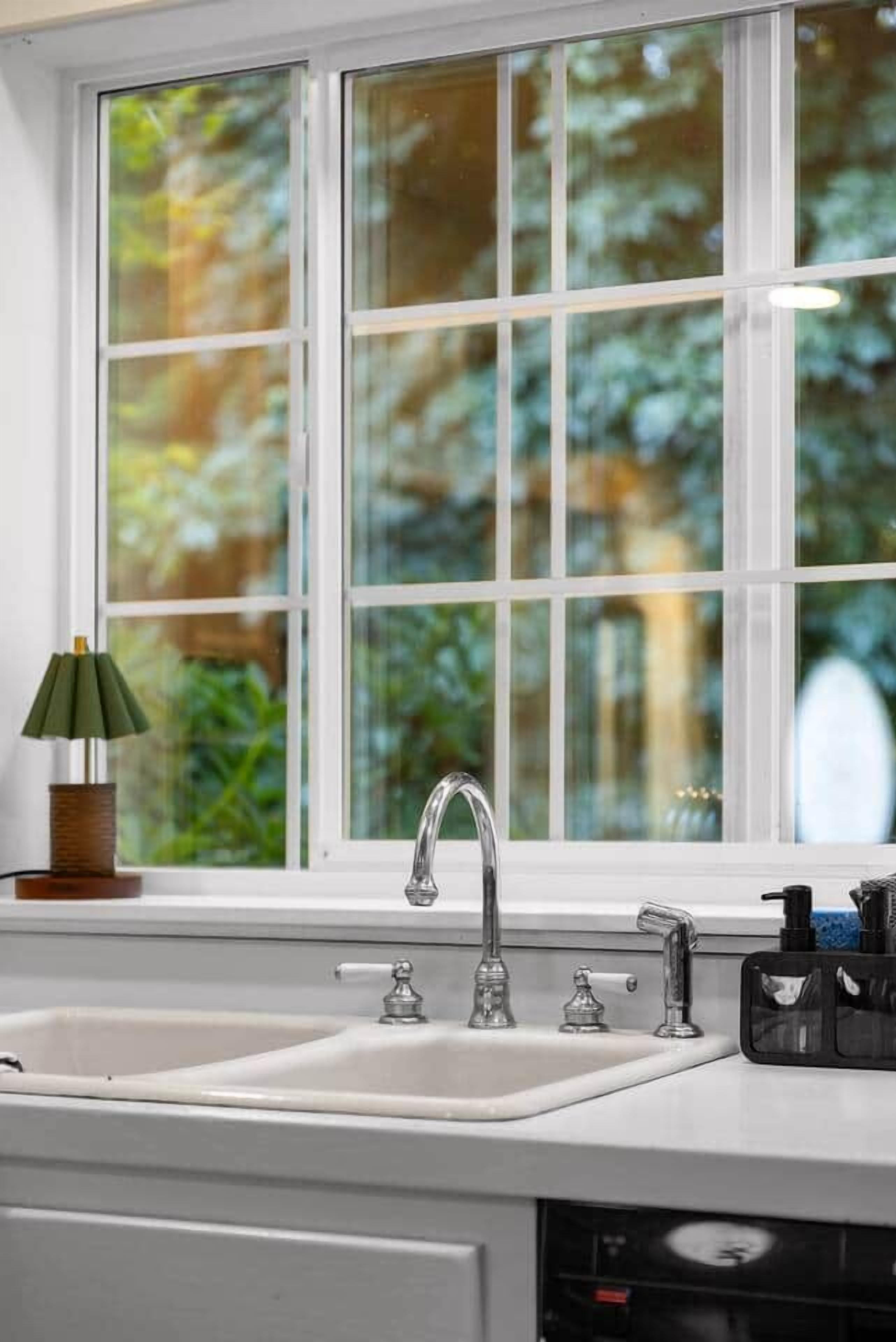 A kitchen with a double sink, a window with a view of greenery, and a lamp on the counter.