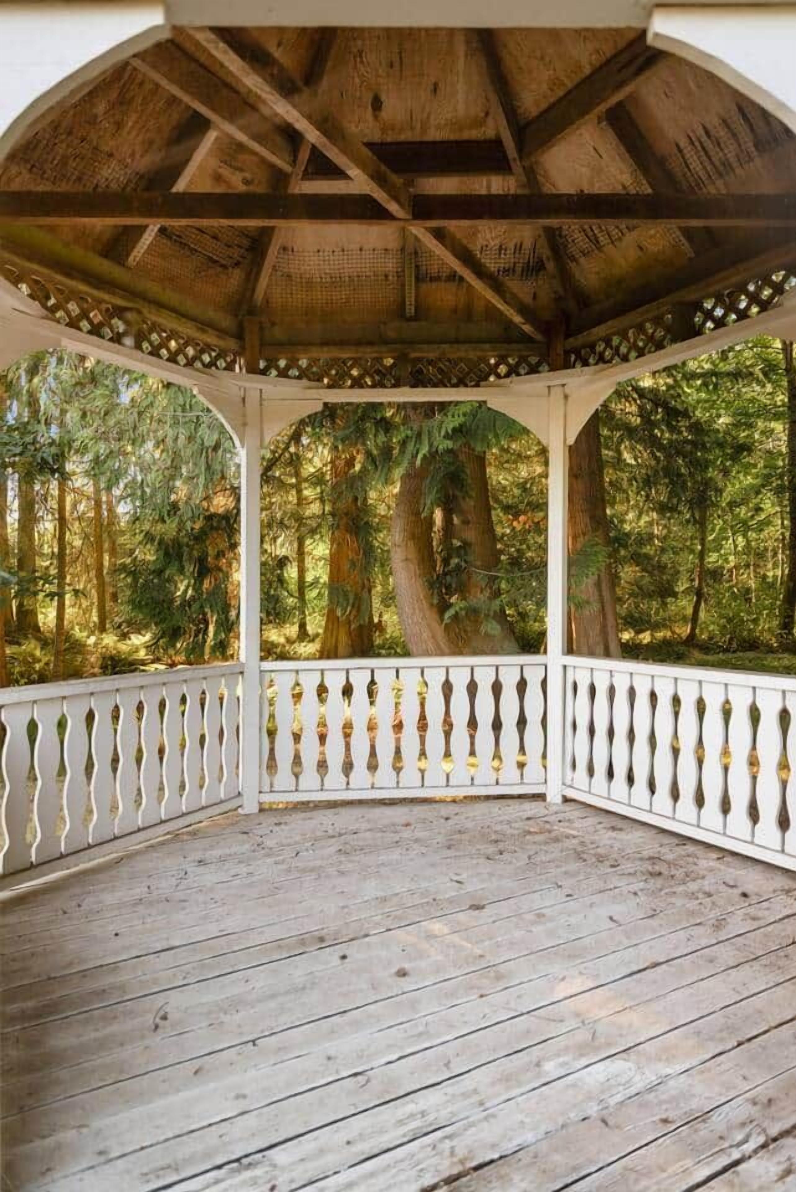 A wooden gazebo with a white balustrade, surrounded by a forested area.