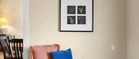 A room with a wooden bench, a framed botanical print on the wall, and a door leading to another room.