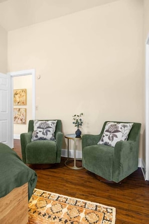 Een kamer met twee groene fauteuils, een klein bijzettafeltje met een vaas en een kamerbreed tapijt met dessin.