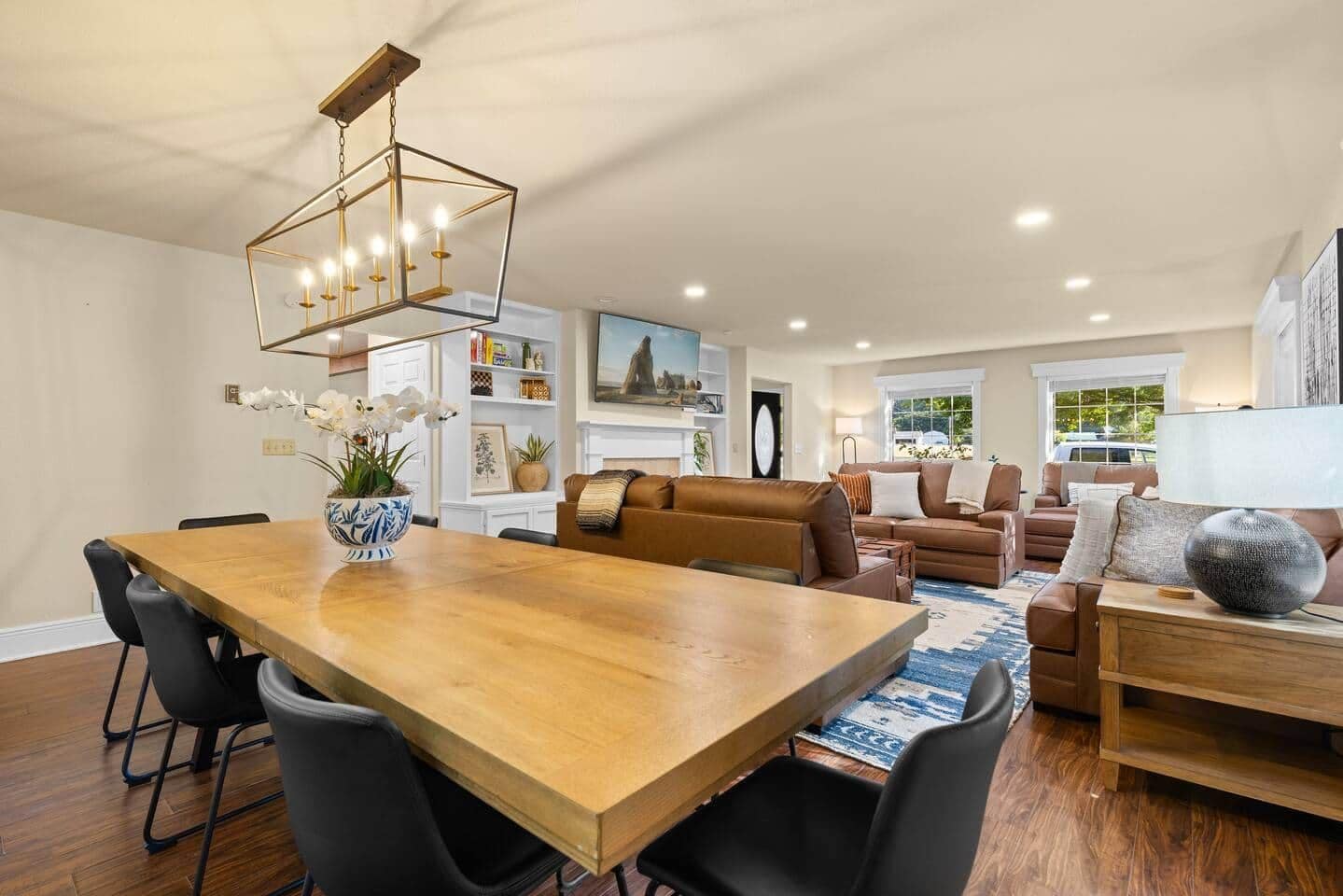 A spacious living area with a wooden dining table, black chairs, a brown leather sofa, and a blue patterned rug.