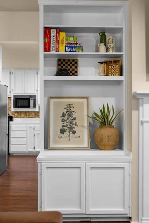 A white cabinet with shelves containing books, a framed botanical print, and a potted plant. - The Farmhouse | Mountain Views + Room to Roam (Port Angeles East)
