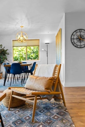 A room with a dining area, a hanging chair, a patterned rug, and a wall clock.