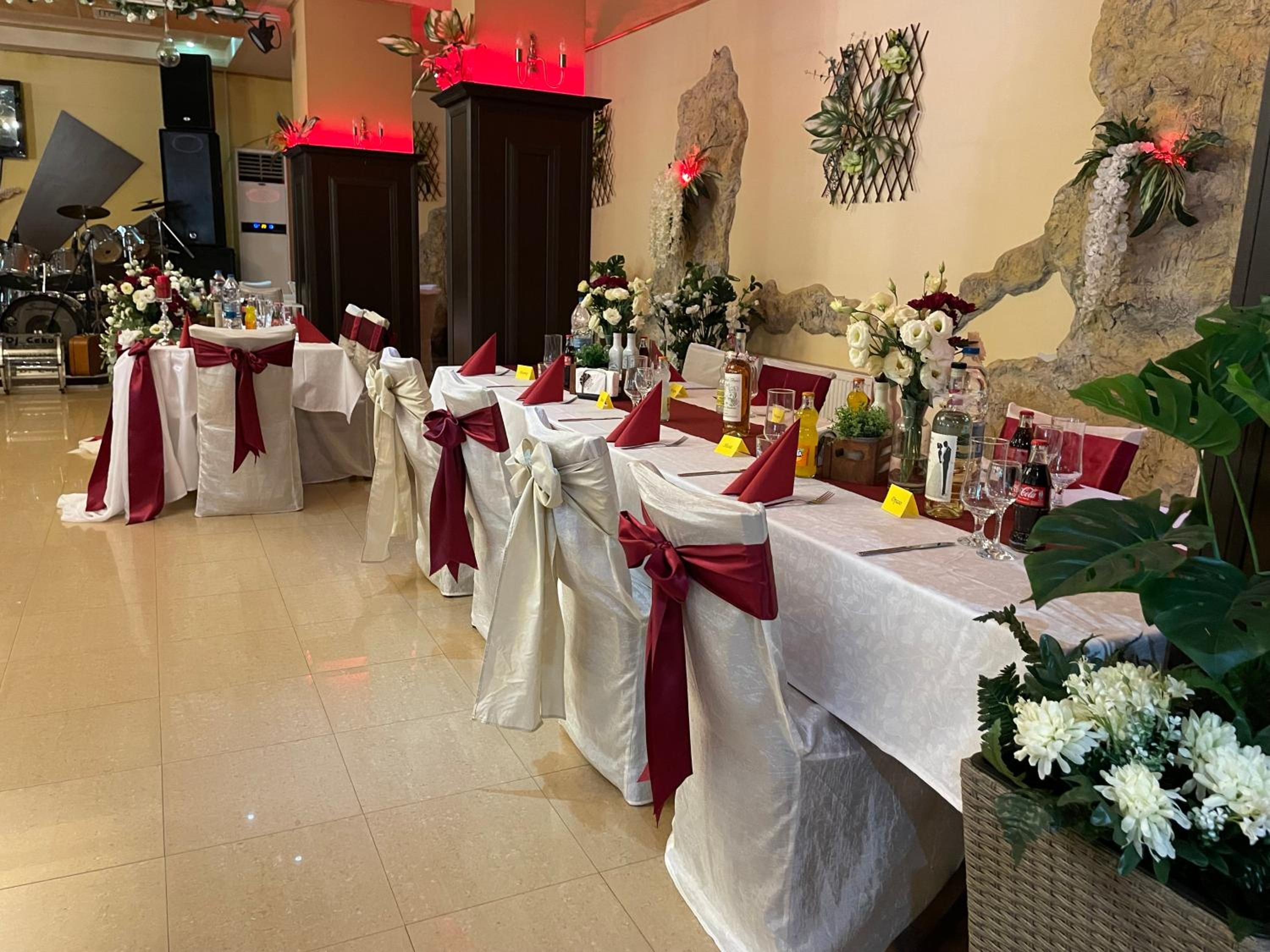 Un salón de banquetes con mesas dispuestas para un evento formal, decorado con centros de mesa florales y cintas rojas.