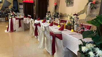 Un salón de banquetes con mesas dispuestas para un evento formal, decorado con centros de mesa florales y cintas rojas.