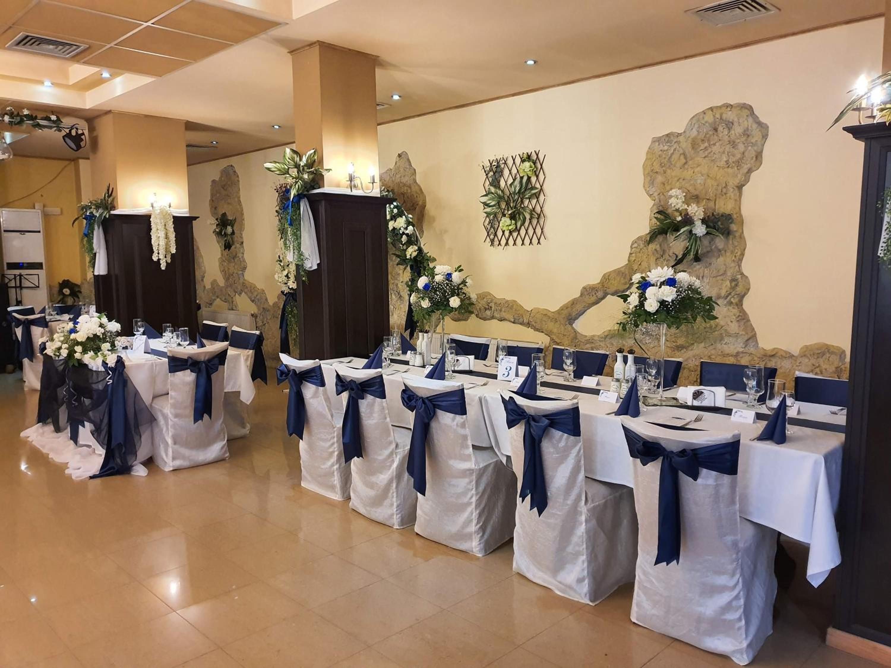 Un salón de banquetes con mesas dispuestas para un evento formal, con manteles blancos y fajas azules.