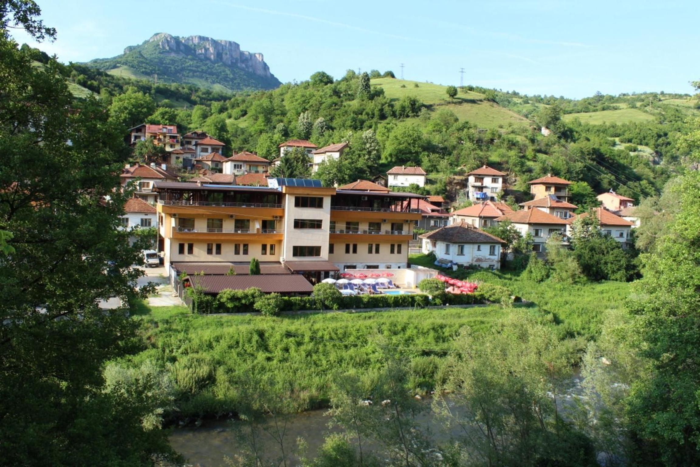 Ein Dorf an einem Hang mit traditionellen Häusern, einem Fluss und einem Berg im Hintergrund.