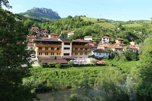 A hillside village with traditional houses, a river, and a mountain in the background.