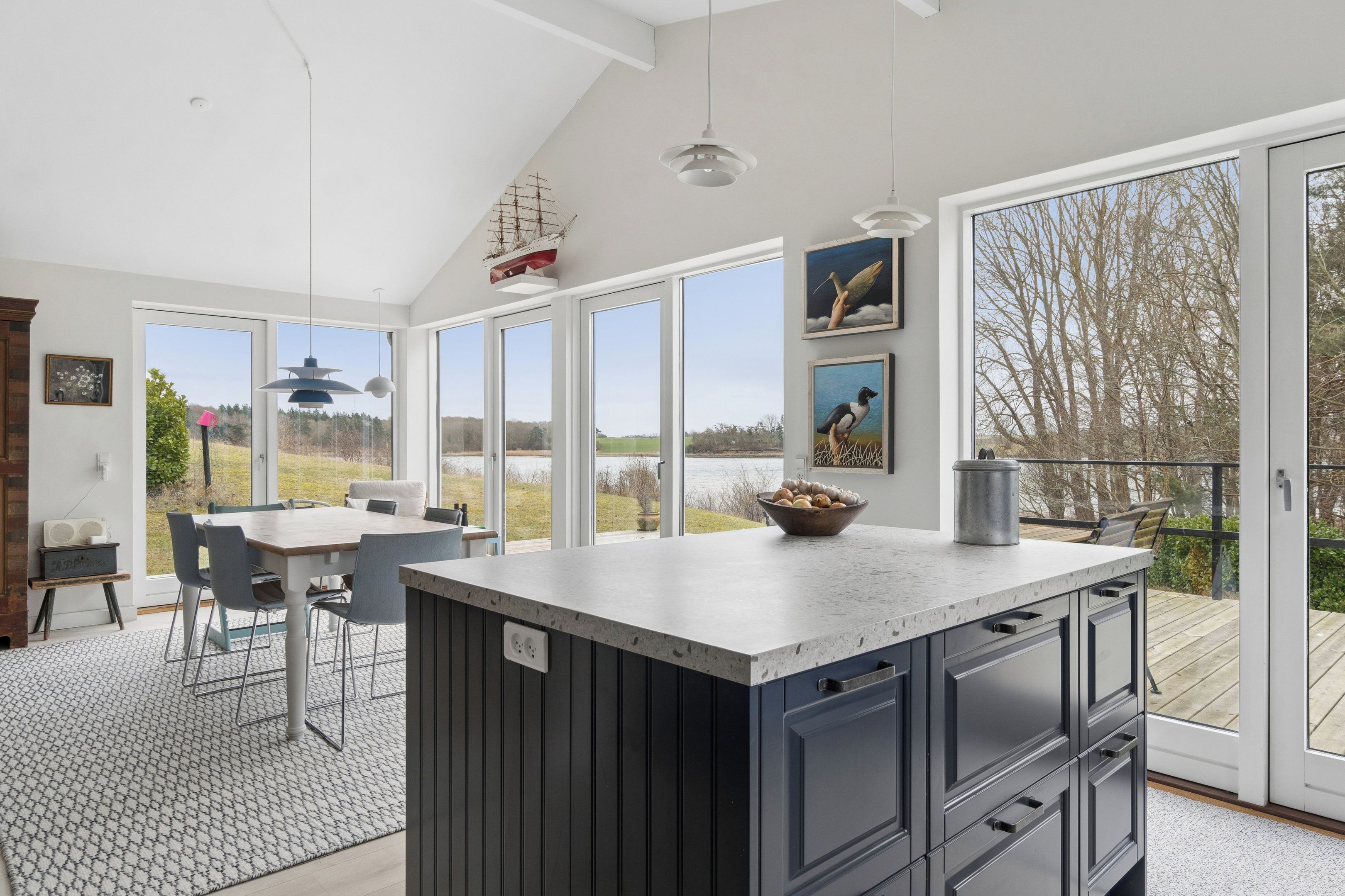 A modern kitchen with a large island, dining area, and large windows offering a view of the outdoors.