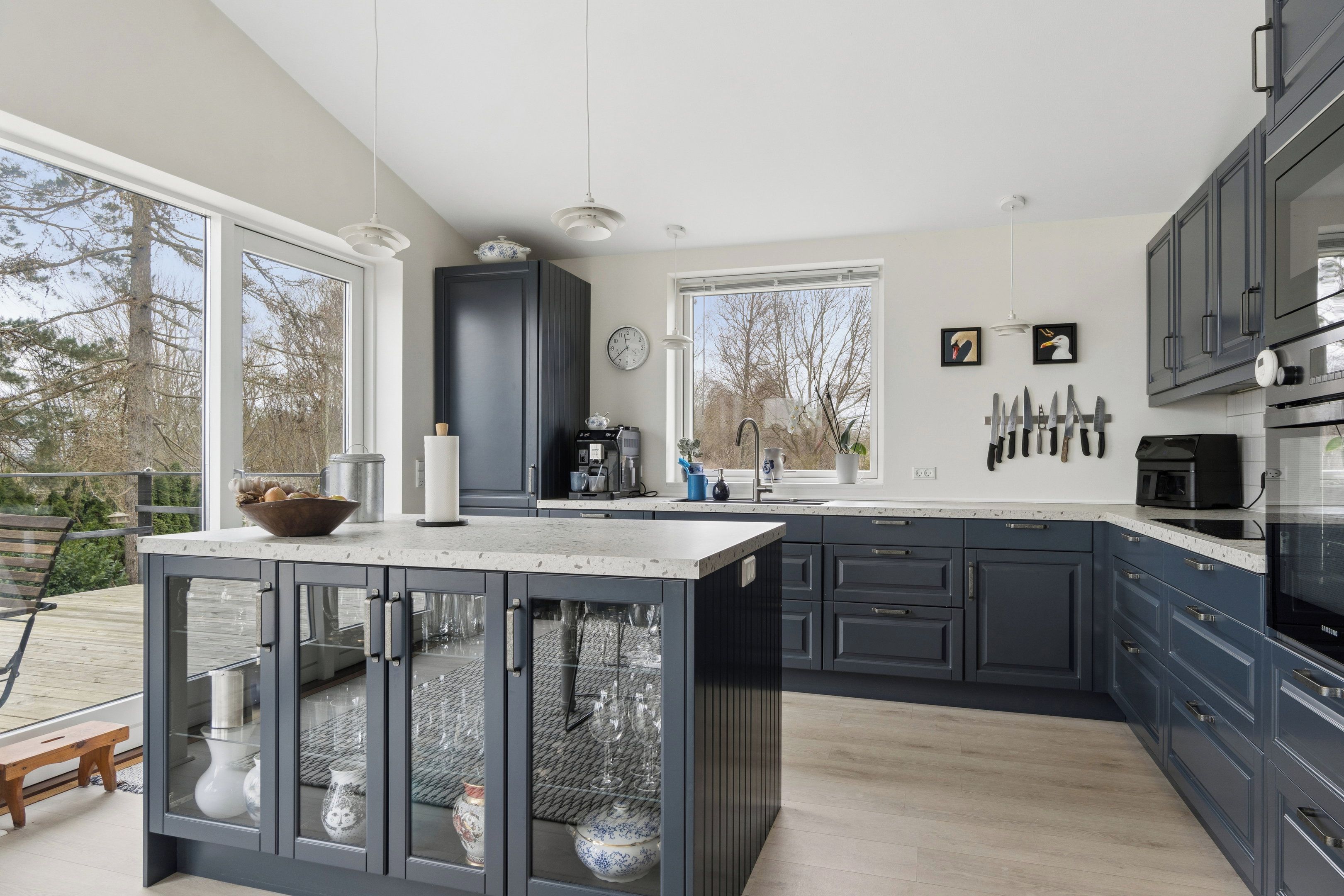 Une cuisine moderne avec des meubles de couleur sombre, un grand îlot central et une vue sur l’extérieur.