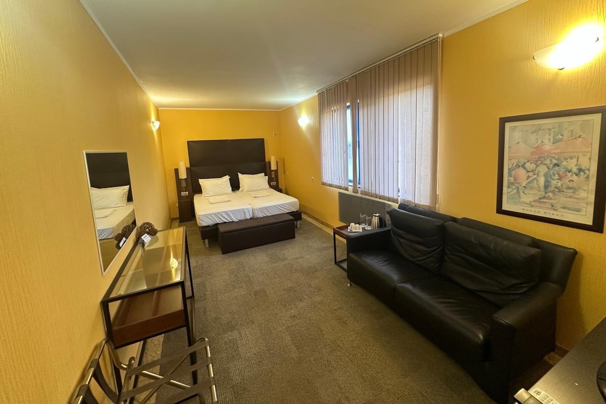 A hotel room with a bed, a black leather sofa, a desk, and a painting on the wall.