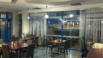 A restaurant with round tables and chairs, a view through large windows, and a modern ceiling design.