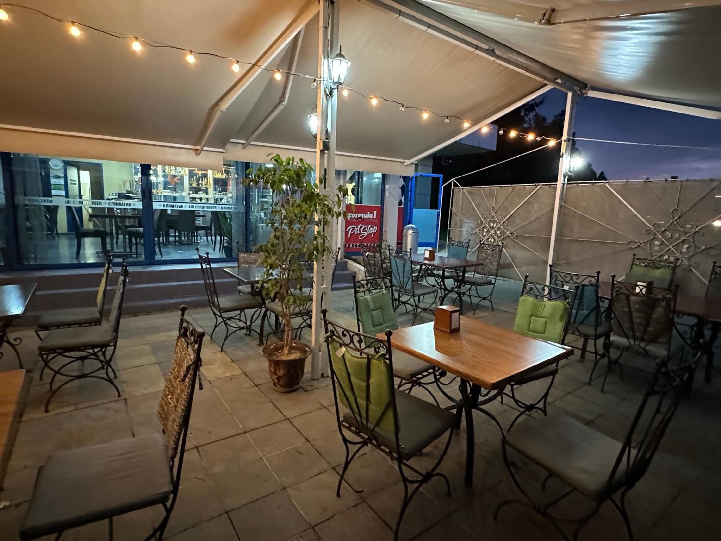 Ein Terrassenbereich im Freien mit Tischen, Stühlen, Lichterketten und einem Blumentopf.