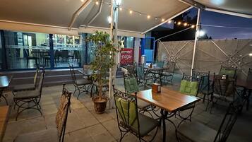 An outdoor patio area with tables and chairs, string lights, and a potted plant.