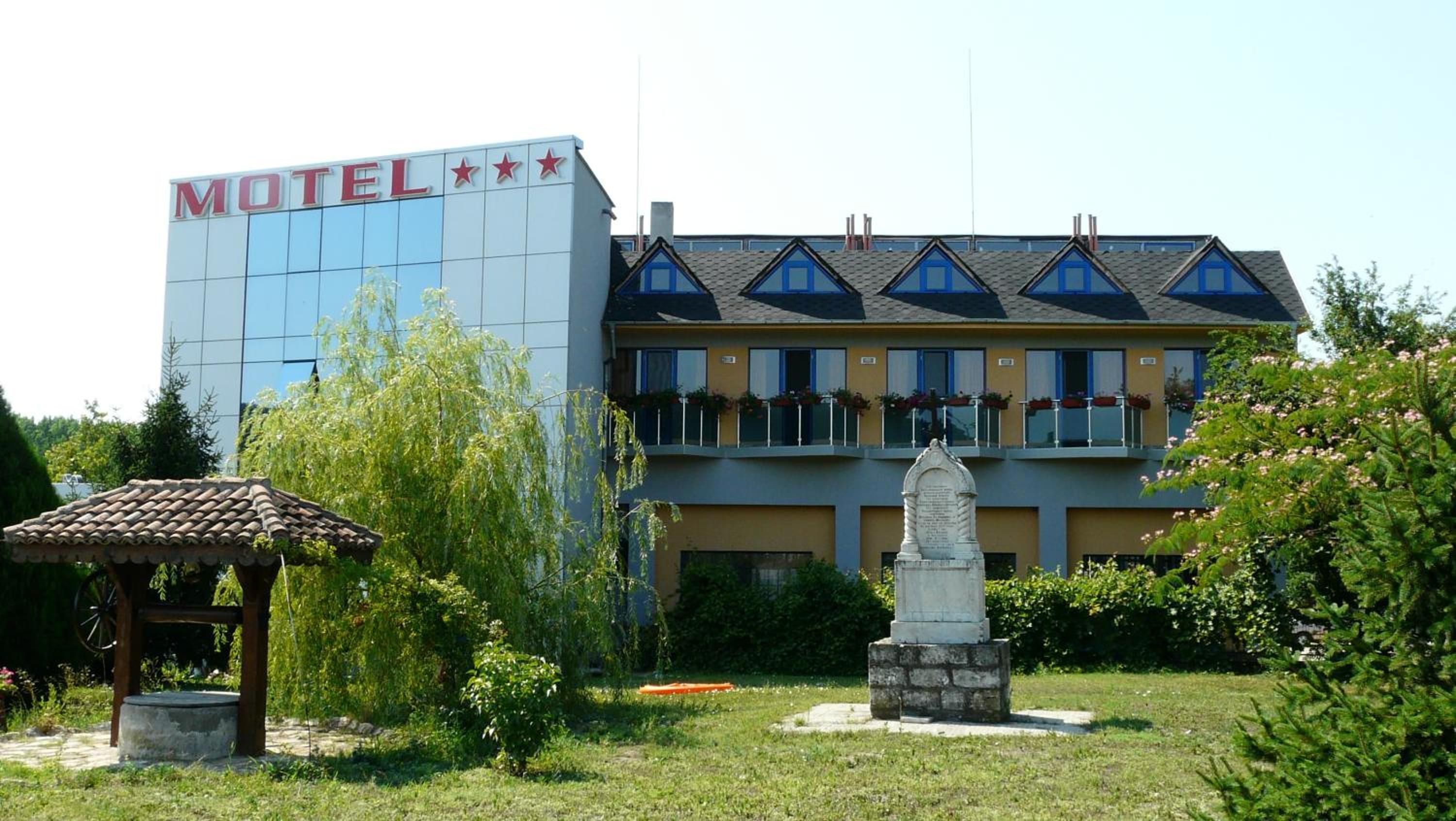 A hotel with a modern exterior, a garden area with a gazebo, and a statue.