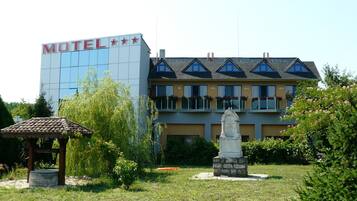 A hotel with a modern exterior, a garden area with a gazebo, and a statue.