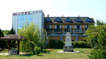 Un hotel con fachada moderna, un jardín con un mirador y una estatua.