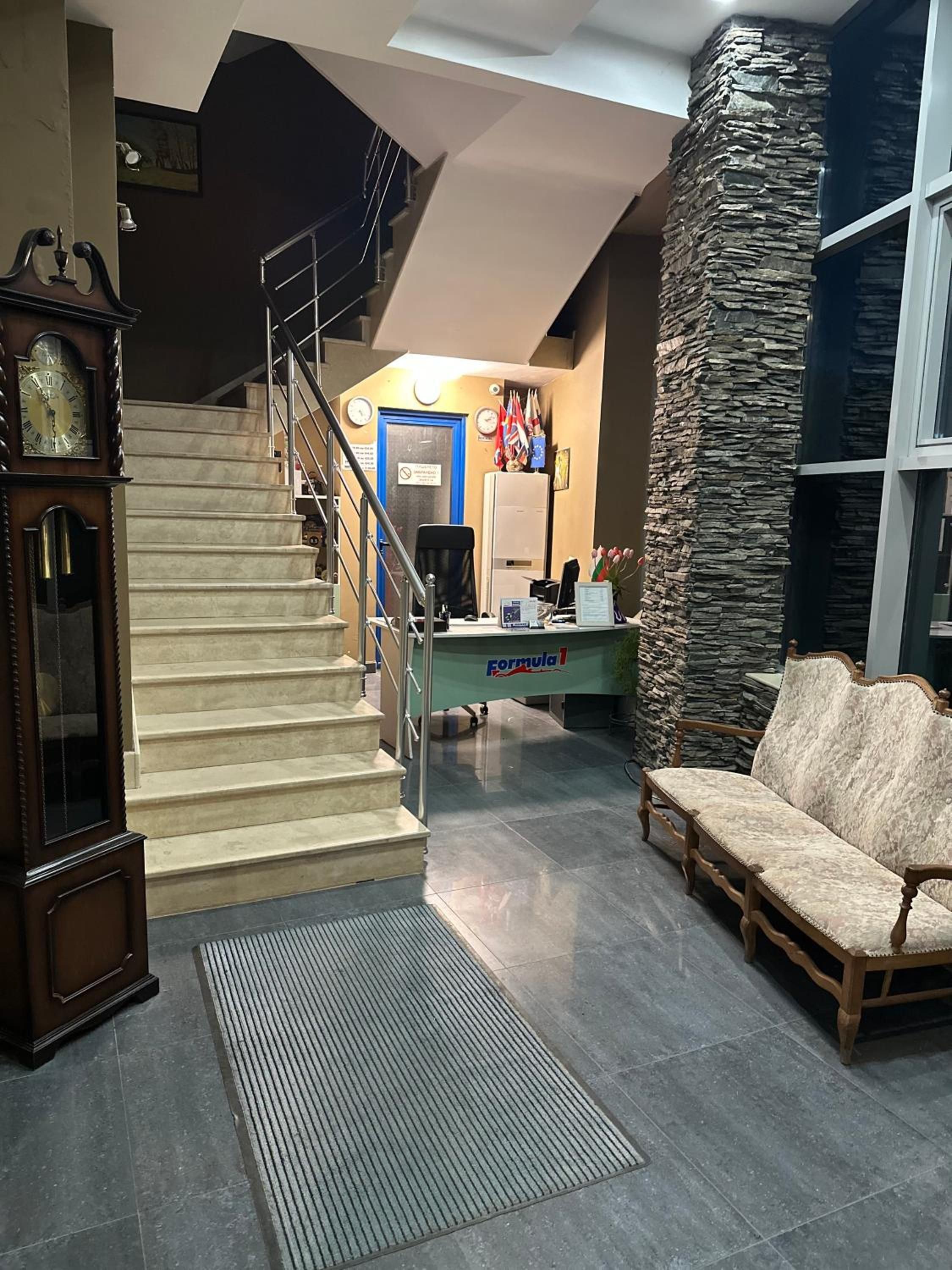 Un área de recepción con escalera, mostrador, sofá y un reloj.