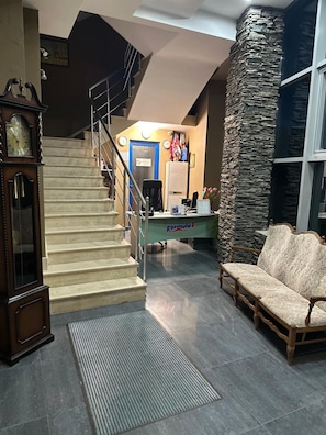 A reception area with a staircase, a reception desk, a sofa, and a clock.