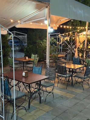 Un patio al aire libre con mesas y sillas, luces colgantes y una zona de estar cubierta.