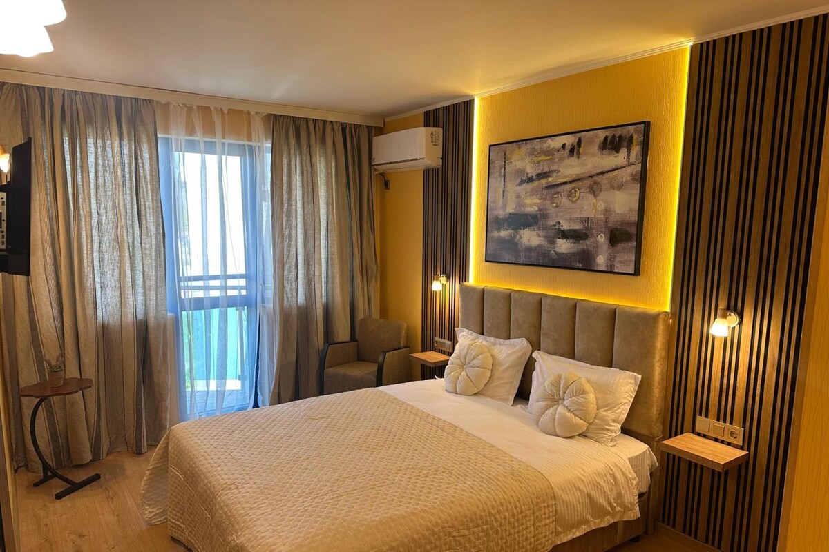 A hotel room with a large bed, a chair, a small table, and a painting on the wall.