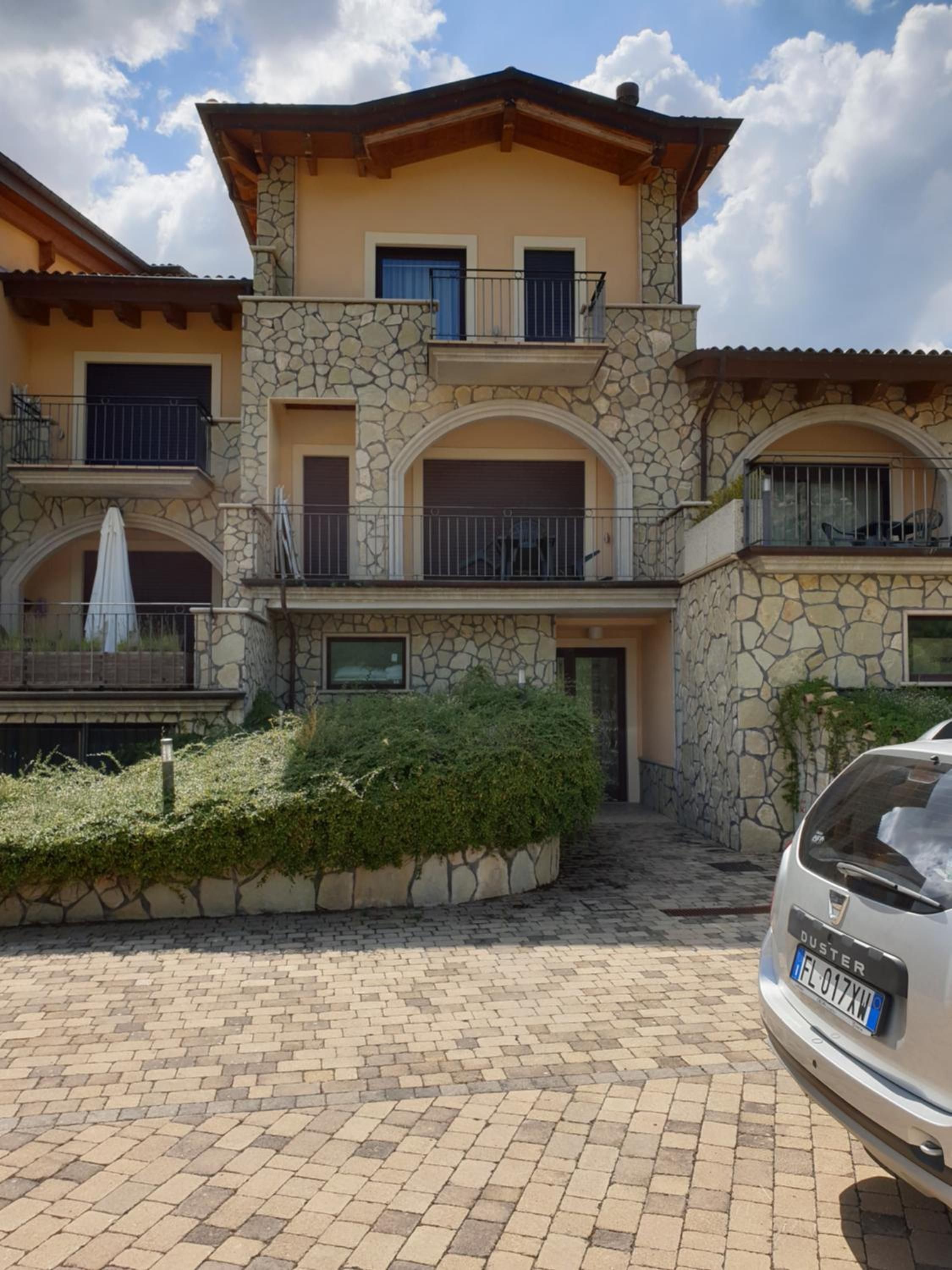 A multi-story building with stone facade, balconies, and a paved driveway.