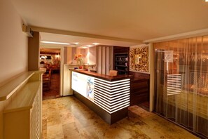 A hotel reception area with a counter, a seating area, and a view of the dining room. - Hotel Leimer Brv U (Lenzing)