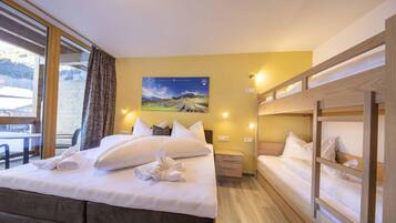 Een hotelkamer met een bed, een nachtkastje, een houten stapelbed, een raam met gordijnen en een schilderij aan de muur.